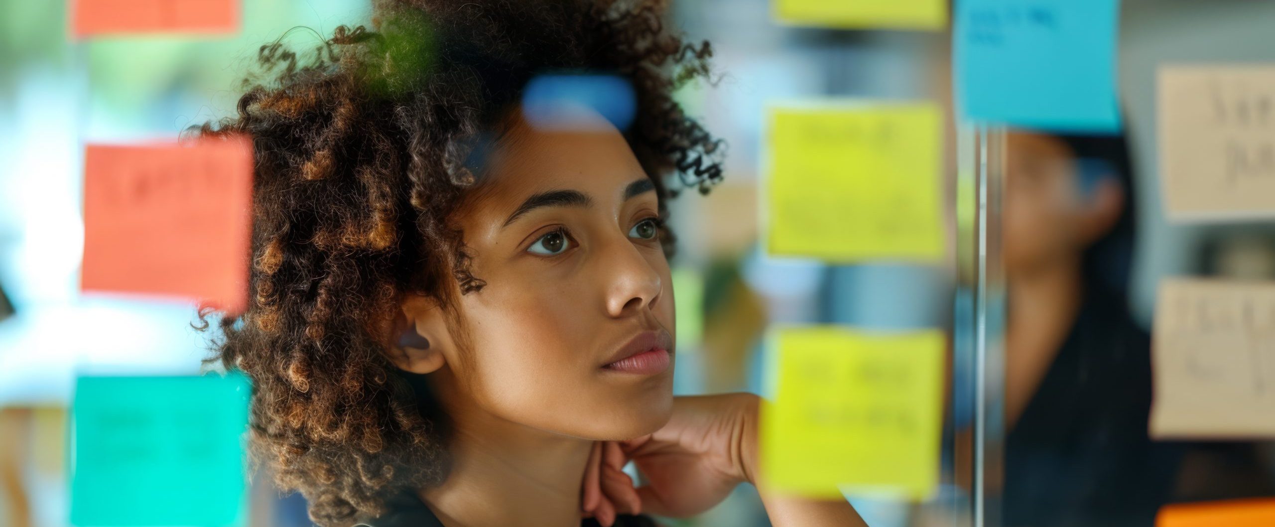 professional woman standing by a glass wall or window covered with colorful post-it notes