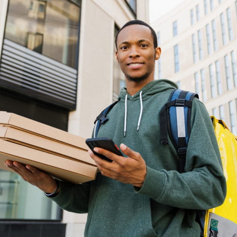 Pizza delivery. An African-American courier holds boxes outside and looks at the camera with a smile.